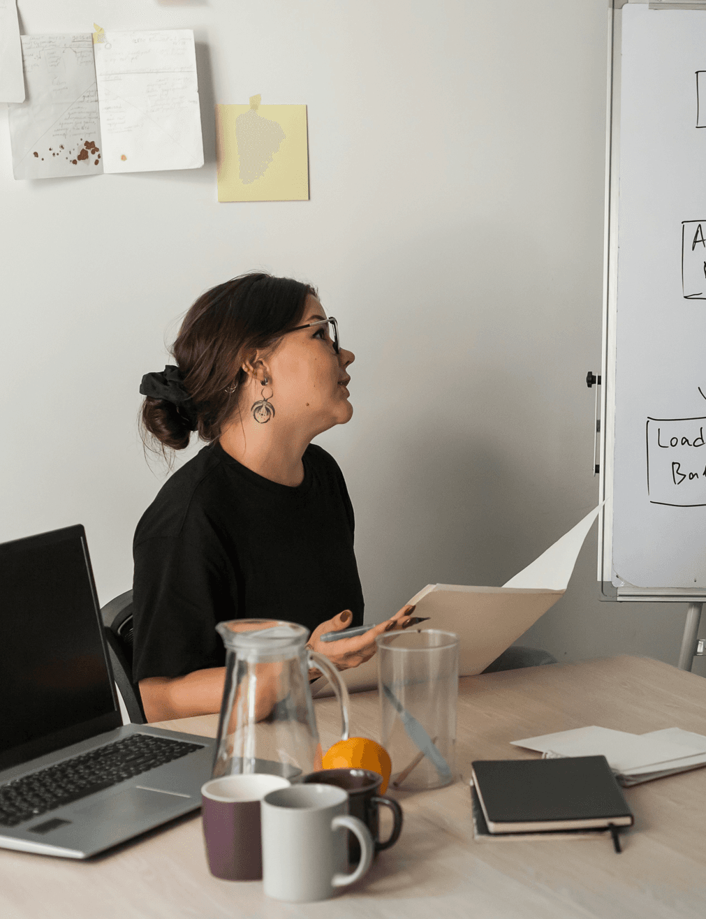 A woman looking at a planning whiteboard with a notebook.